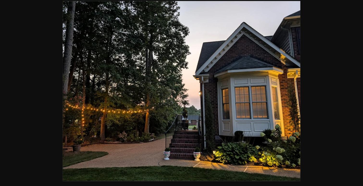 Brick exterior and bay window of the home at dusk with string lights